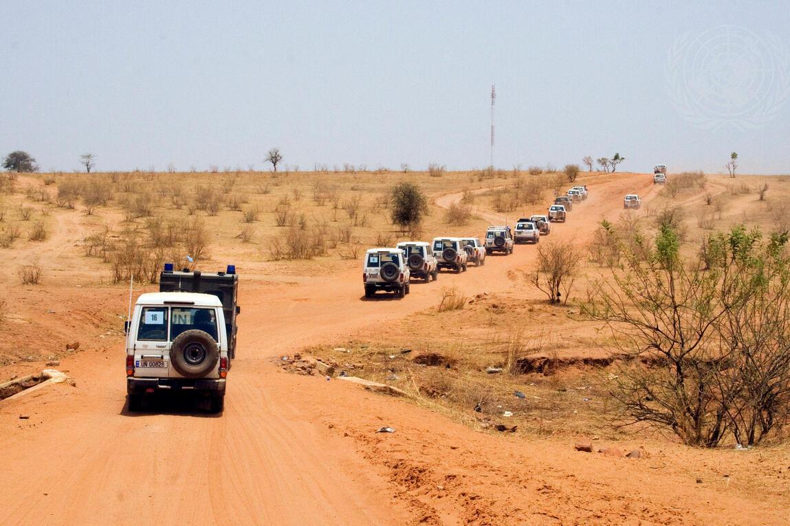 A convoy of UN four wheel drive vehicles along a red dirt road.